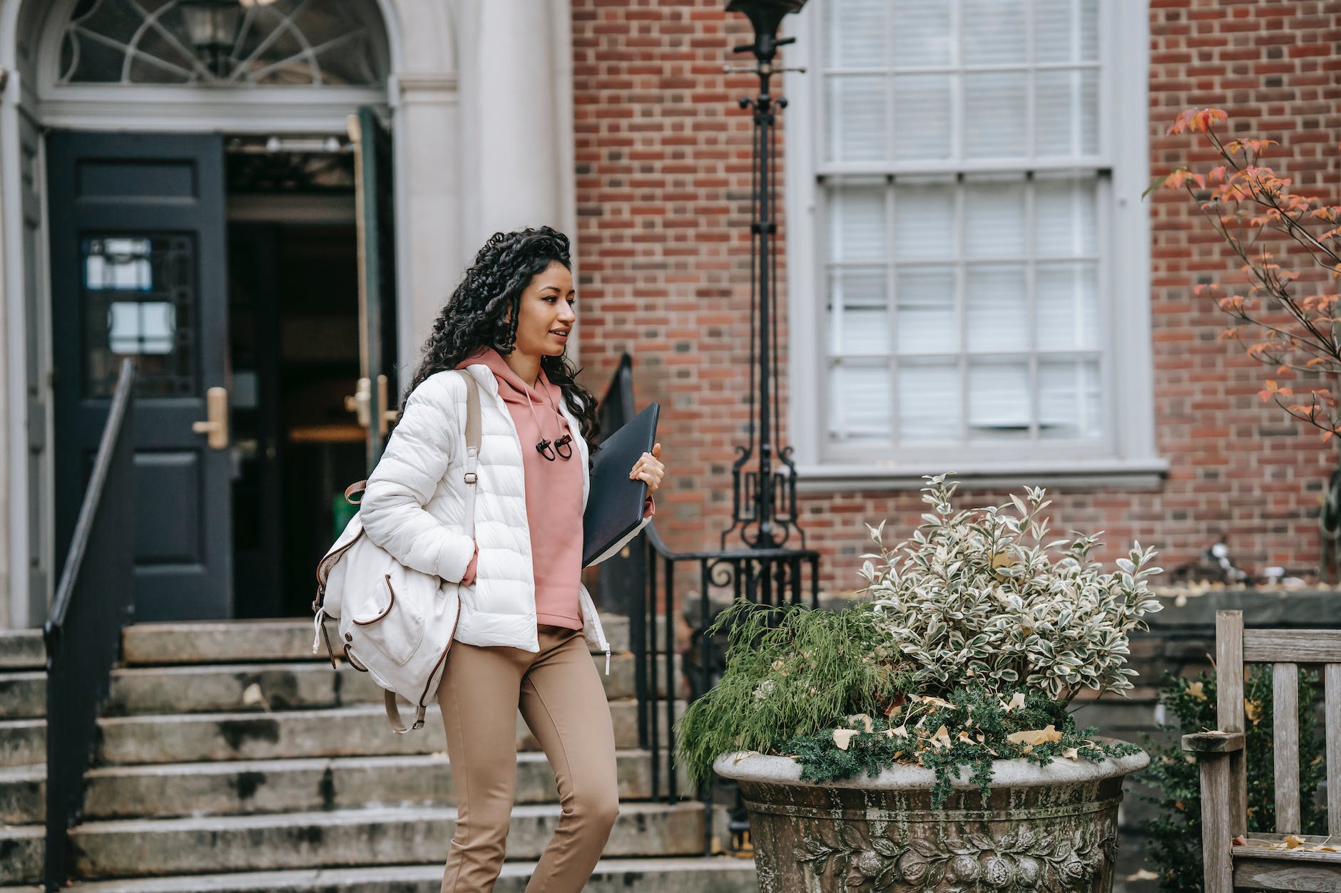 a woman walking on a college campus with a white jacket on 